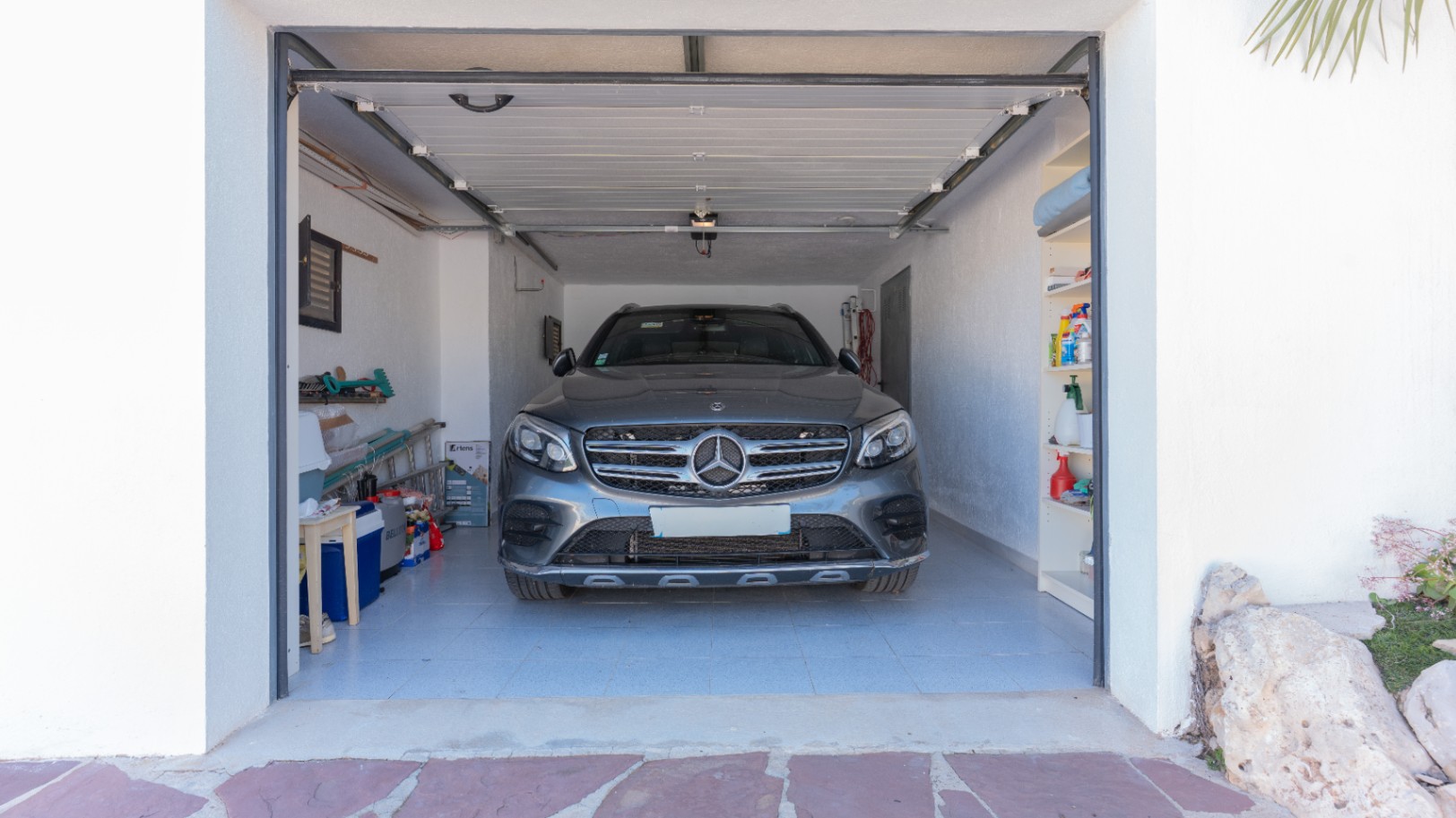 Privégarage met tegelvloer en automatische sectionaaldeur, voorzien van zijdelingse opbergrekken voor een georganiseerde opslagruimte.