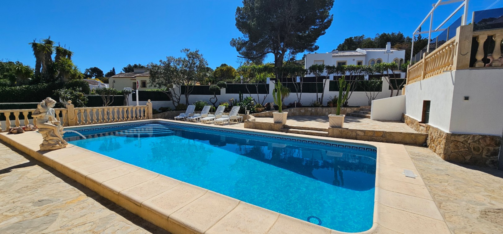 Rechthoekig zwembad met inlooptrap, omgeven door een ruim stenen terras met ligbedden en een mediterrane tuin met volwassen beplanting.