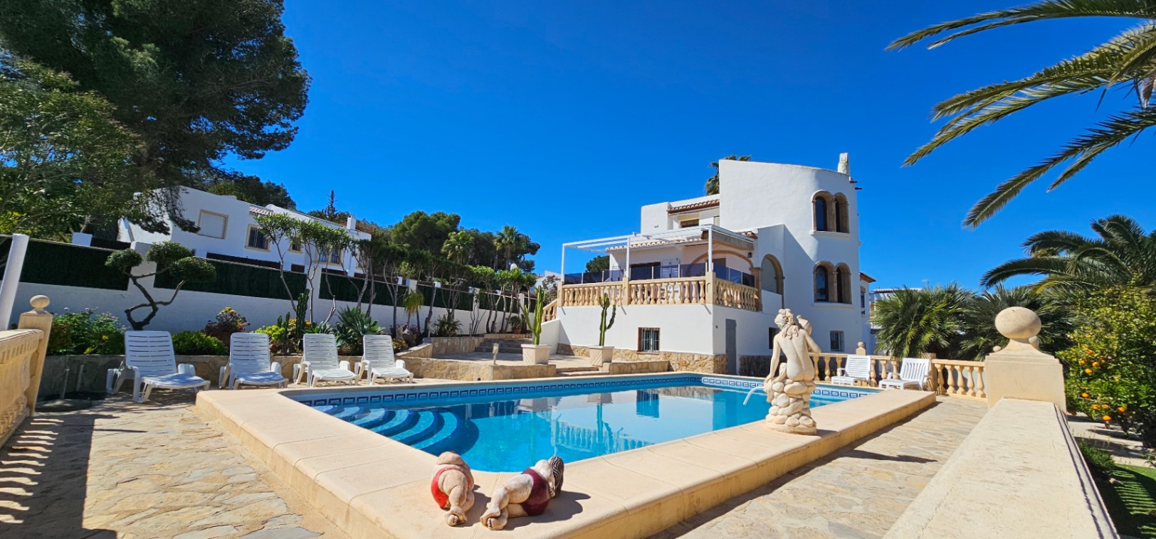 Rechthoekig zwembad met Romeinse trap, omgeven door een stenen terras, witte ligbedden en een mediterrane villa met een karakteristieke ronde toren.