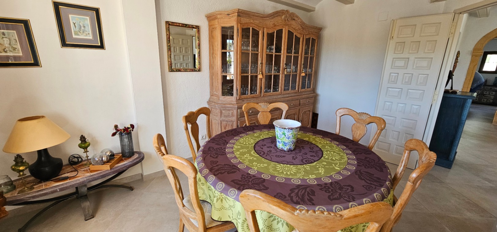 Rustieke eethoek met een ronde tafel, bewerkte houten stoelen en een grote klassieke servieskast. De ruimte is voorzien van keramische tegels en traditionele decoratie.
