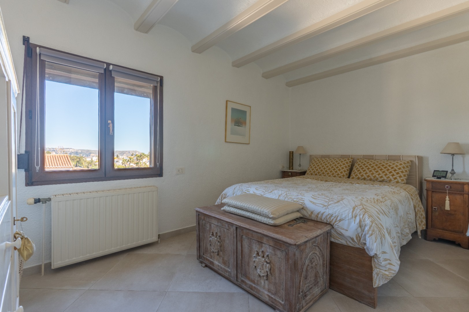 Slaapkamer met zichtbare plafondbalken, tegelvloer en een rustieke houten kist. Voorzien van centrale verwarming en een venster met uitzicht op de omgeving.