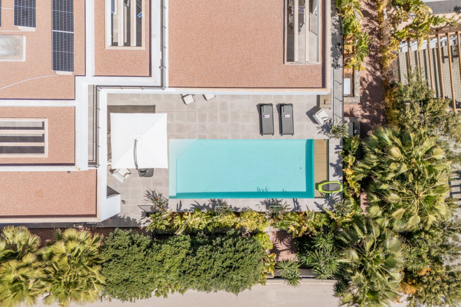 Bovenaanzicht van het rechthoekige zwembad en het betegelde terras, omgeven door mediterrane beplanting en zonnepanelen op het dak.