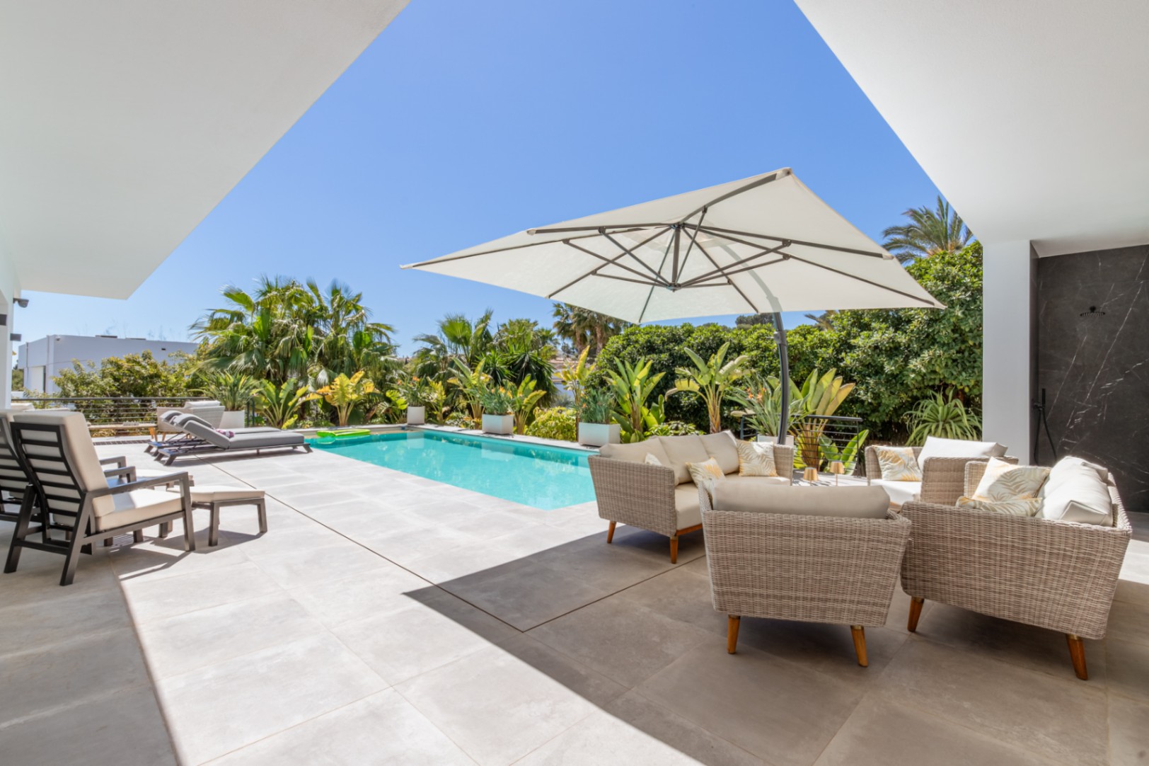 Buitenterras met rechthoekig zwembad, wicker loungeset onder een parasol en volwassen mediterrane beplanting die zorgt voor volledige privacy.