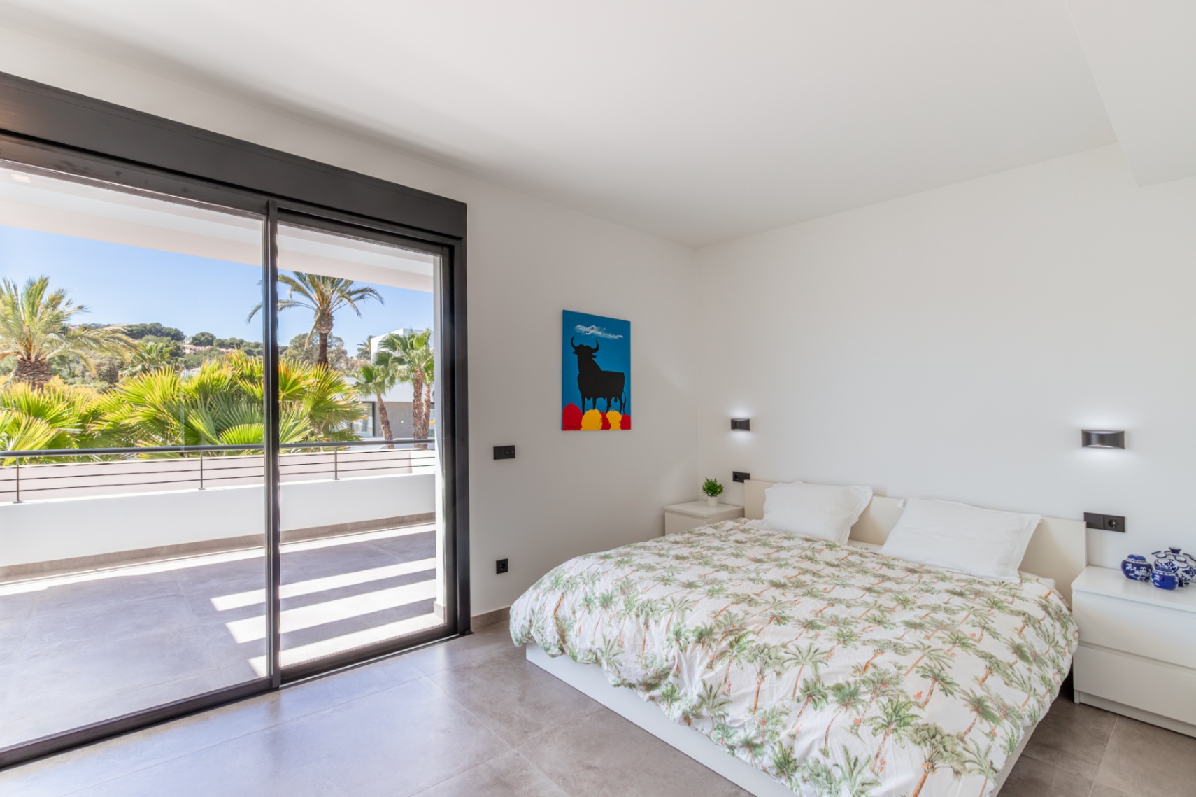 Lichte slaapkamer met directe toegang tot een privéterras via grote glazen schuifdeuren. Grijze tegelvloer en minimalistische inrichting met wandverlichting.
