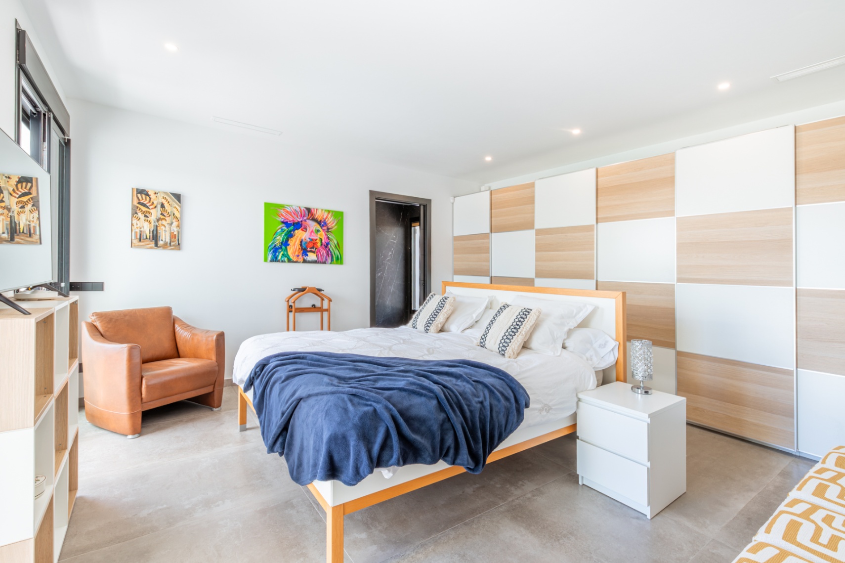 Lichte slaapkamer met een kamerhoge inbouwkast in een dambordpatroon van hout en wit, grijze tegelvloer en een stijlvolle leren fauteuil.