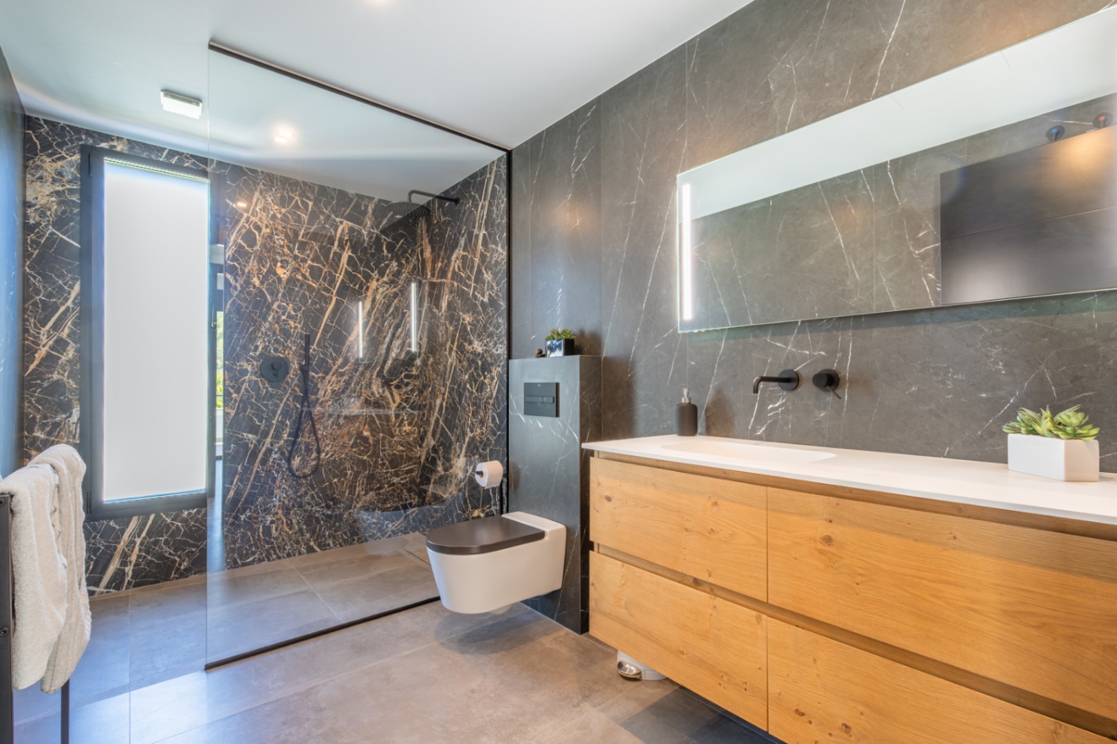 Moderne badkamer met donkere marmerlook wandtegels, een natuurlijk houten wastafelmeubel en een ruime inloopdouche met glazen wand en zwarte kranen.