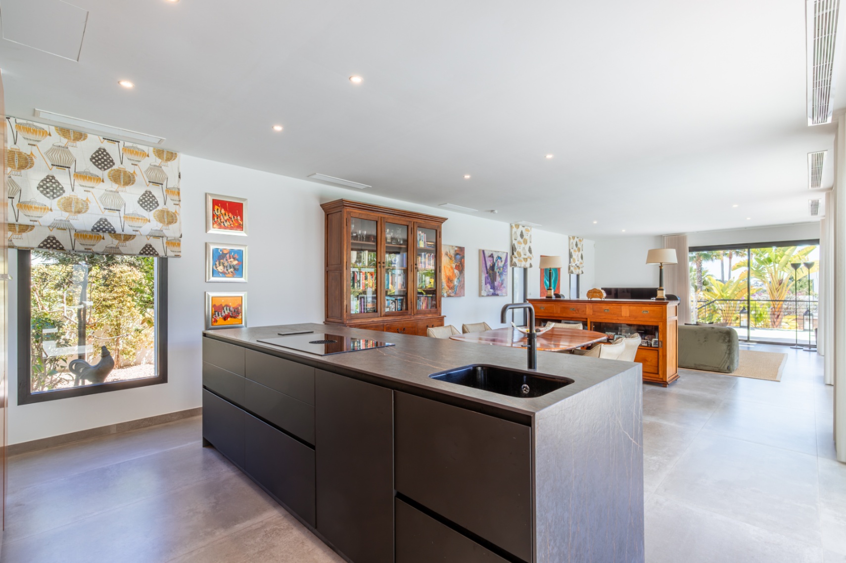 Moderne keuken met een donkerstenen kookeiland, geïntegreerde spoelbak en inductiekookplaat, grenzend aan de lichte woonkamer met toegang tot het terras.