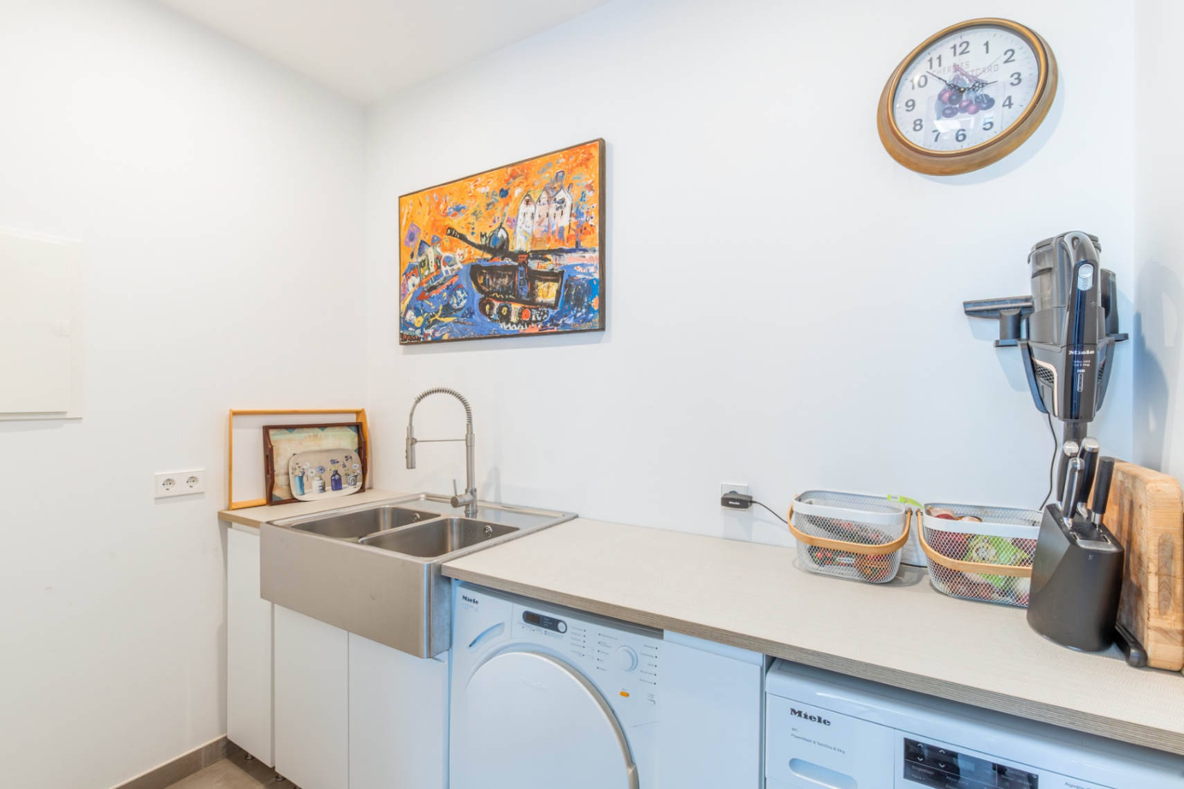 Praktische wasruimte uitgerust met hoogwaardige Miele-apparatuur, een dubbele roestvrijstalen spoelbak en een ruim werkblad in een lichte, moderne omgeving.