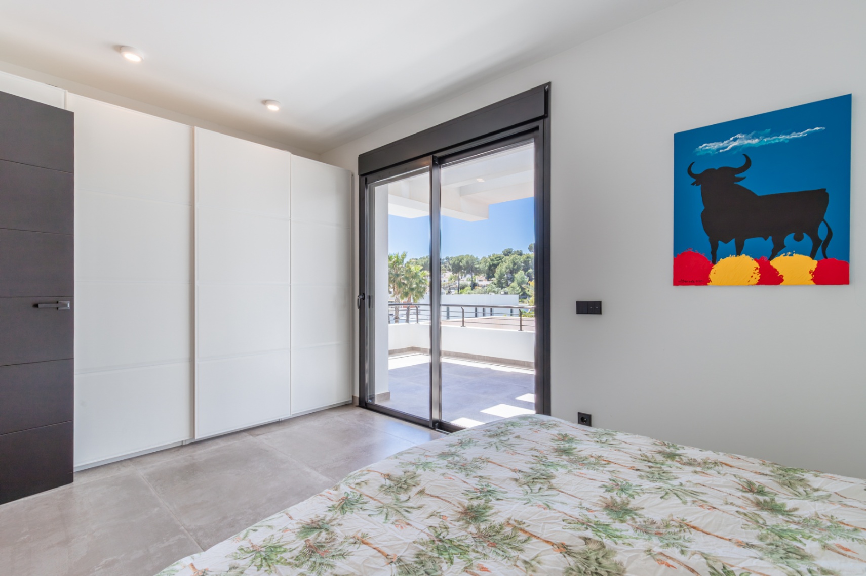 Slaapkamer met witte inbouwkasten en directe toegang tot een privéterras via een glazen schuifdeur, afgewerkt met een moderne tegelvloer.