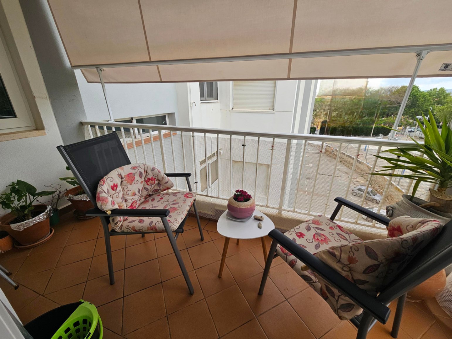 Balkon met terracotta tegelvloer, voorzien van een uitschuifbaar zonnescherm en buitenmeubilair bestaande uit twee stoelen en een kleine bijzettafel.