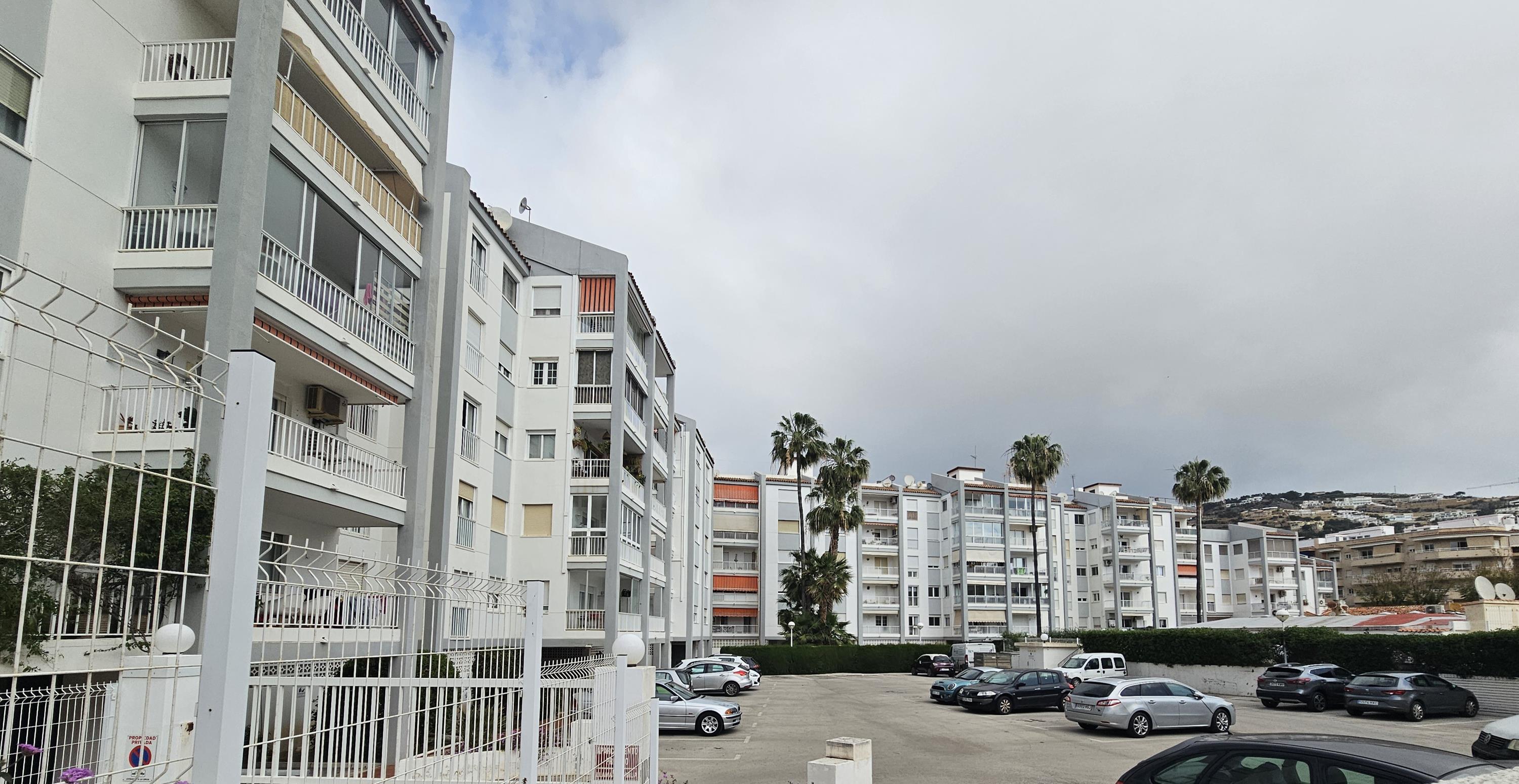 Buitenaanzicht van het wooncomplex met privébalkons, een omheinde gemeenschappelijke parkeerplaats en palmbomen in Jávea.