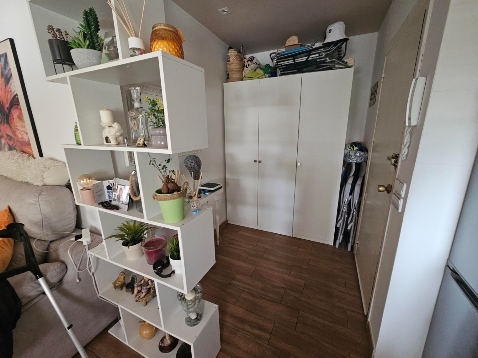 Functionele hal met houtlook tegelvloer, een witte driedeurs kledingkast en een asymmetrische open kast die als roomdivider fungeert.