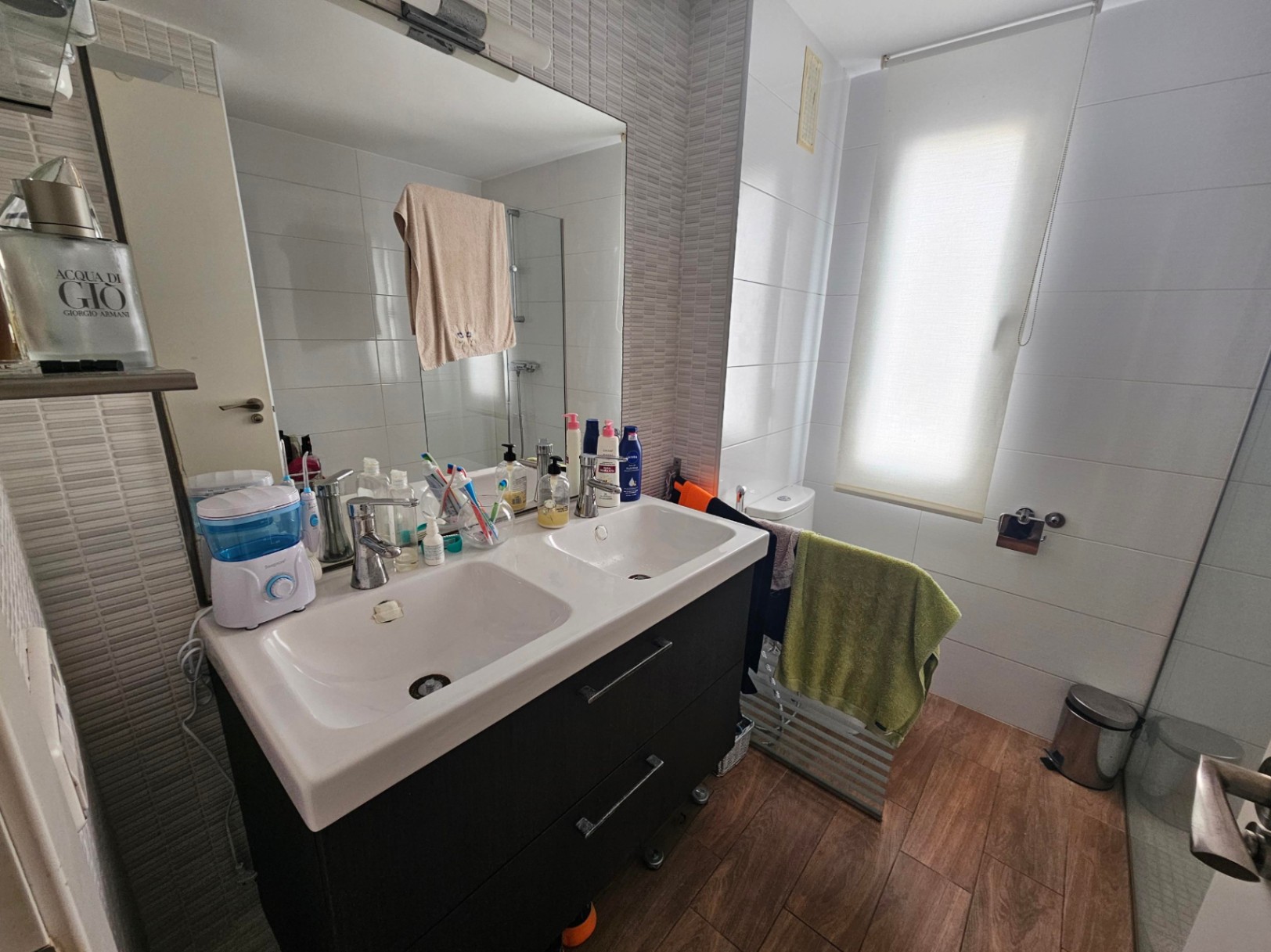 Moderne badkamer met dubbel wastafelmeubel in donkere uitvoering, keramische vloer met houtlook en neutrale wandtegels met natuurlijk lichtinval.