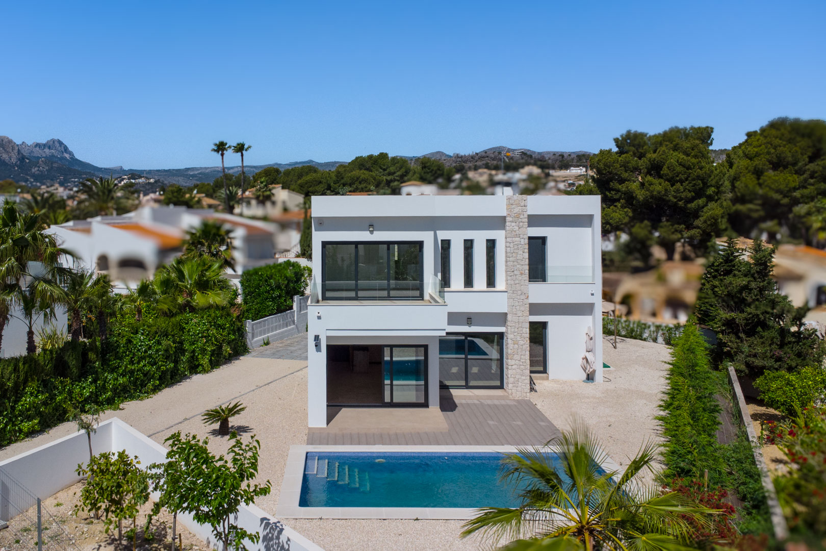 Buitenaanzicht van de moderne witte villa met natuurstenen kolom, rechthoekig zwembad en ruime terrassen met glazen balustrades.