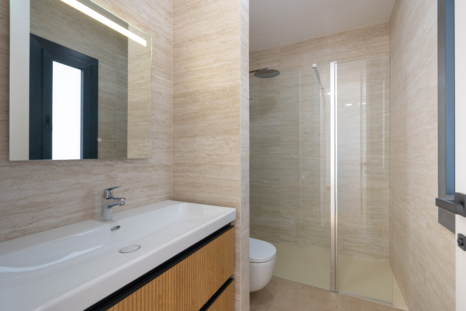 Designbadkamer met porseleinen wandtegels in steenlook, een hangend wastafelmeubel met geribbeld hout en een inloopdouche met glazen wand en regendouche.