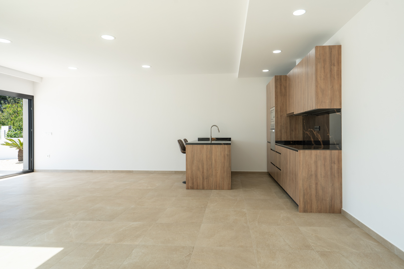 Designkeuken met houten afwerking, donker geaderd werkblad en kookeiland, geïntegreerd in een open ruimte met grootformaat porseleinen vloertegels.