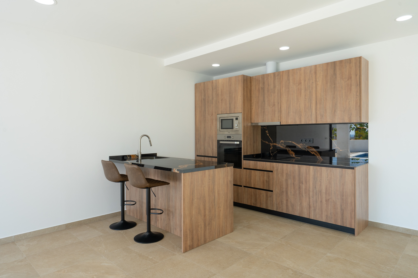 Designkeuken met houten fronten, zwart marmerlook werkblad met aders en een kookeiland met barkrukken. Voorzien van inbouwapparatuur en inbouwspots in het plafond.