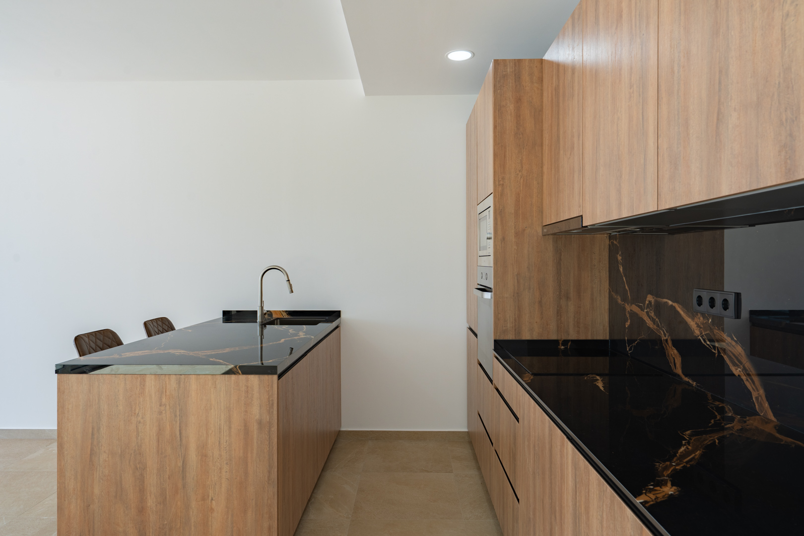 Designkeuken met kasten in houtafwerking, donkere werkbladen met aders en een kookeiland met geïntegreerde spoelbak en minimalistische kraan.