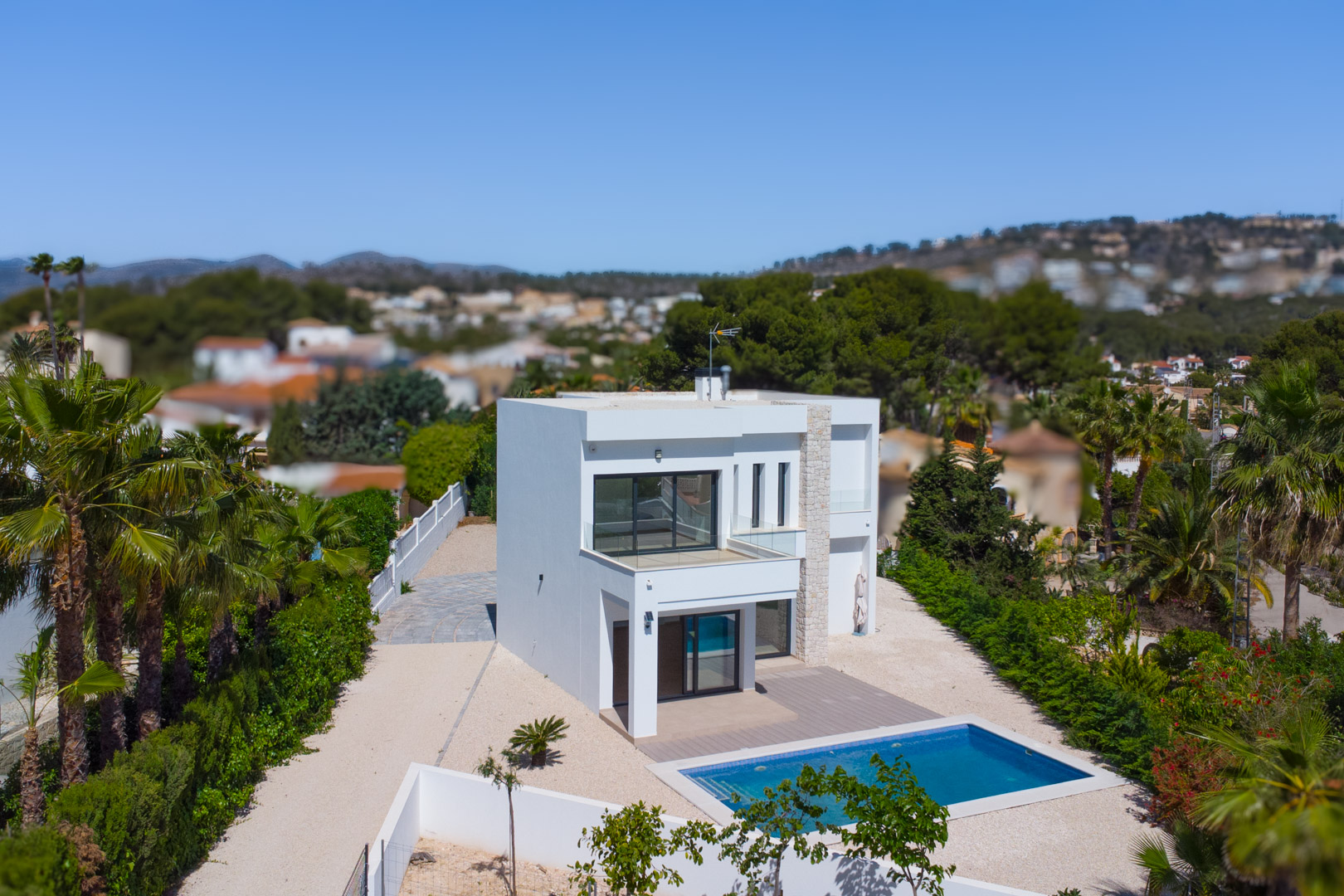 Exterieur van de moderne villa met witte gevel, natuurstenen accenten, rechthoekig zwembad en terrassen met glazen balustrades op een riant vlak perceel.