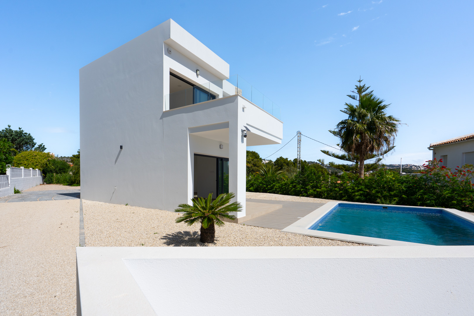 Exterieur van de moderne witte villa met rechthoekig zwembad, onderhoudsvriendelijke grindtuin en ruime terrassen met glazen balustrades.