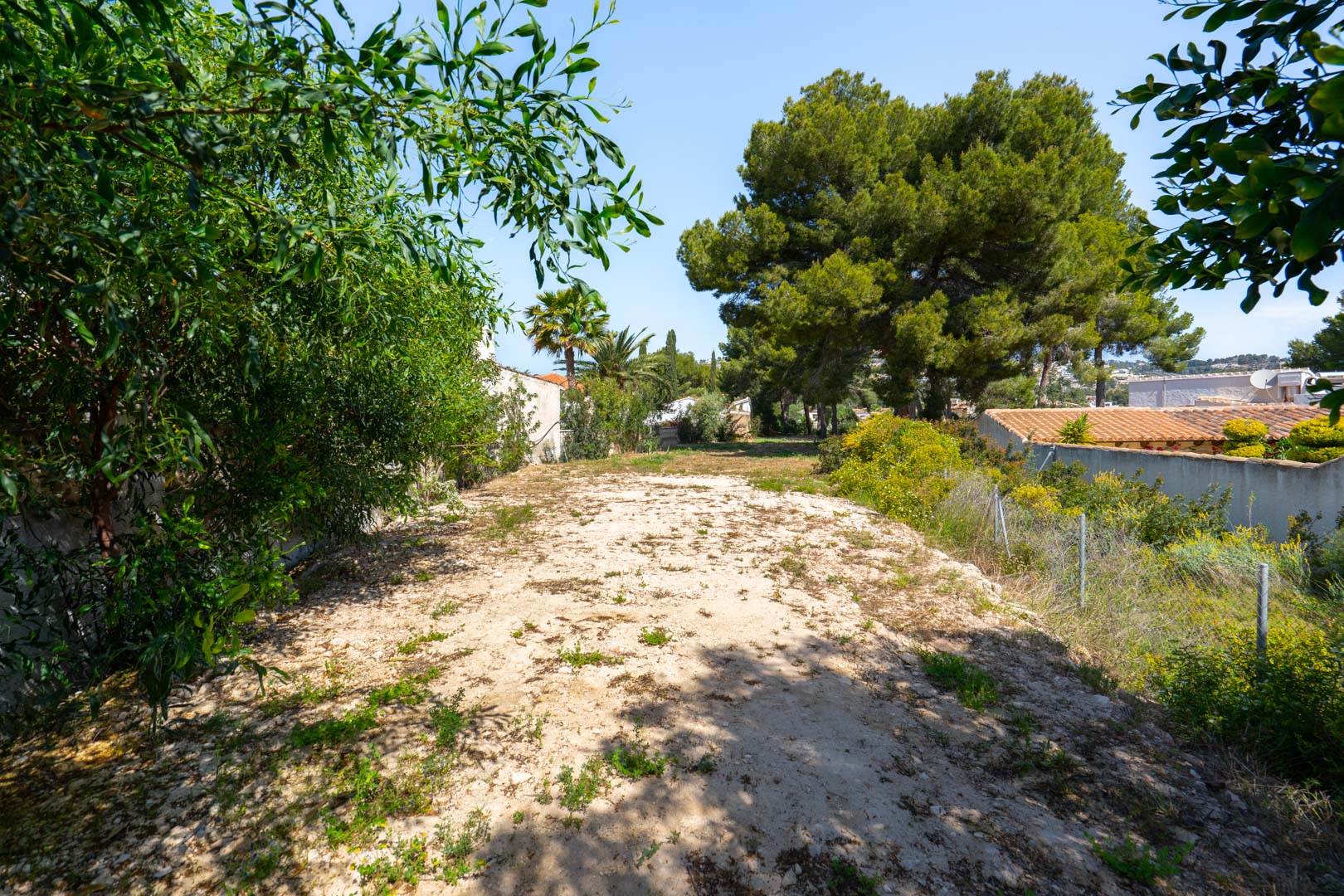 Groot vlak perceel van 900 m2 aan de achterzijde van de villa, omzoomd door volwassen bomen en groen, met diverse mogelijkheden voor bijgebouwen.