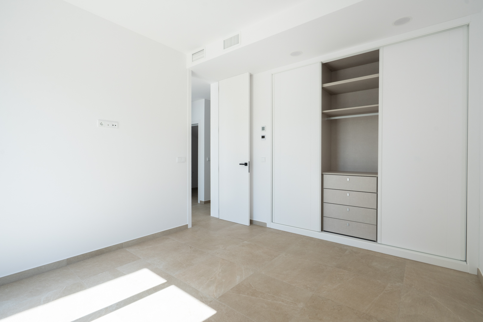 Lichte slaapkamer met witte inbouwkasten met schuifdeuren, een georganiseerd interieur met lades en planken, en een grootformaat porseleinen tegelvloer.