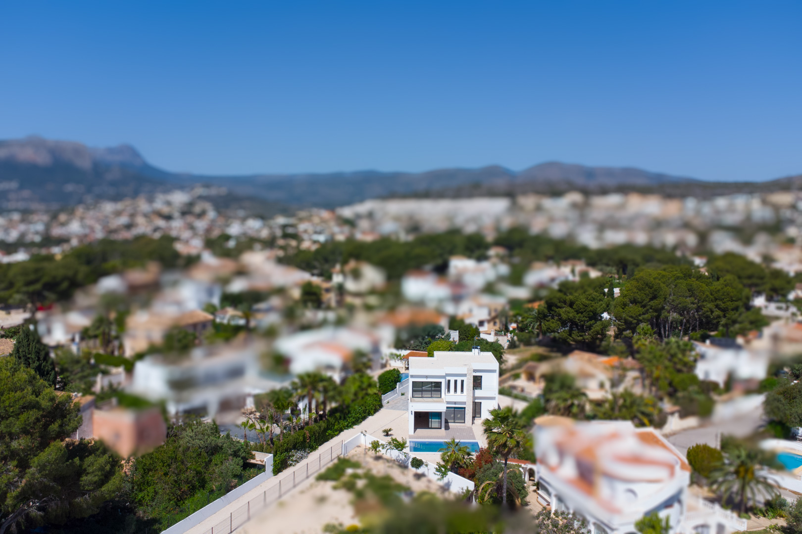 Luchtfoto van de moderne villa met witte gevel en zwembad, die de ligging in het mediterrane landschap van Benissa en de nabijheid van de kust toont.