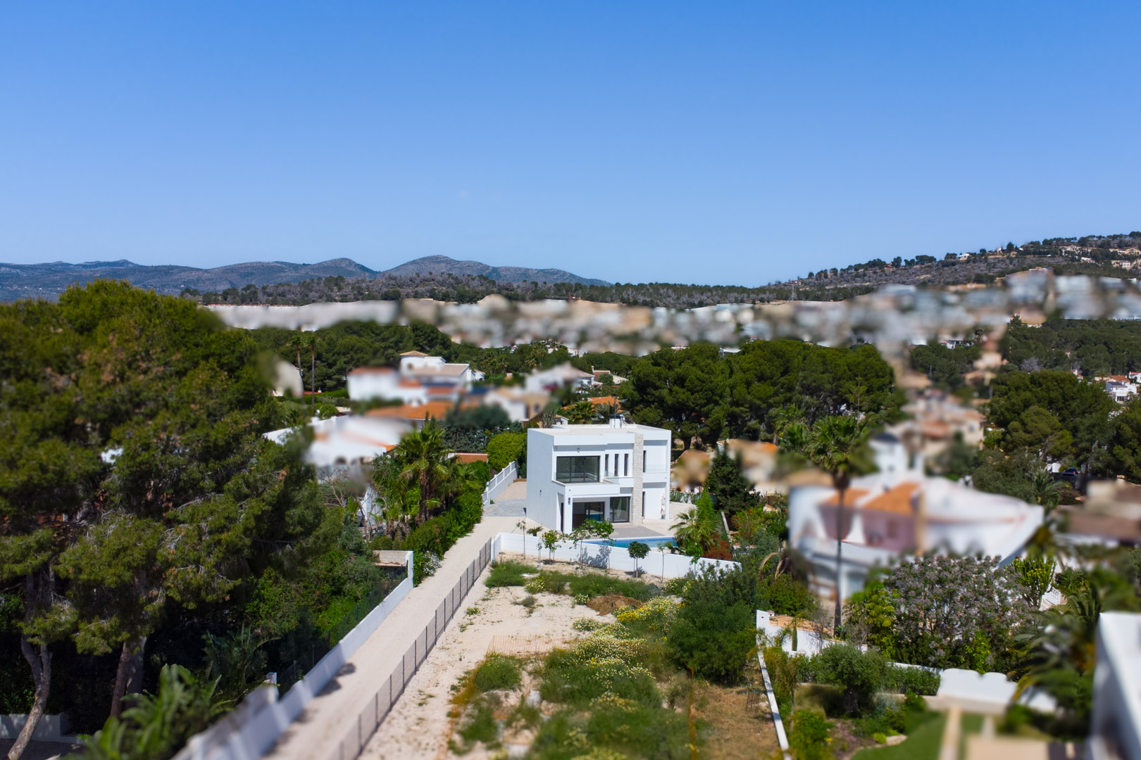 Luchtfoto van de moderne witte villa op een uitgestrekt vlak perceel, omringd door mediterrane pijnbomen en met uitzicht op de bergen.