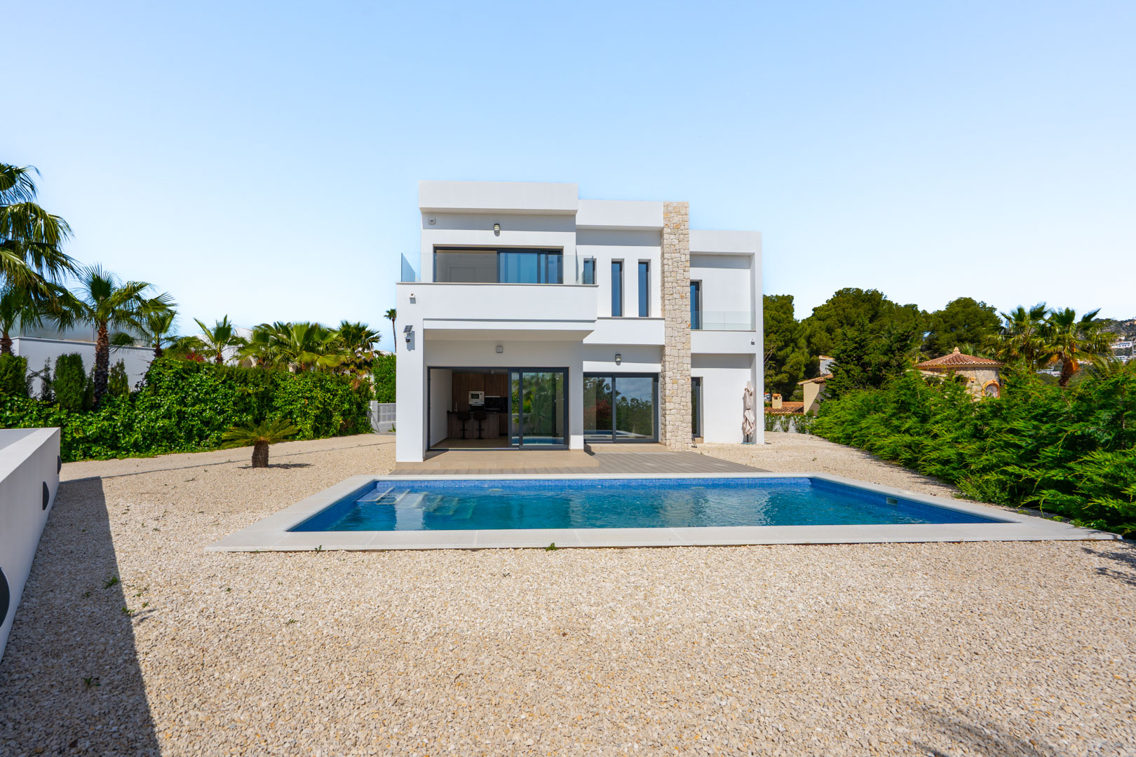 Moderne villa met twee verdiepingen, witte gevel met natuurstenen accenten, rechthoekig zwembad en grindtuin omgeven door mediterrane begroeiing.