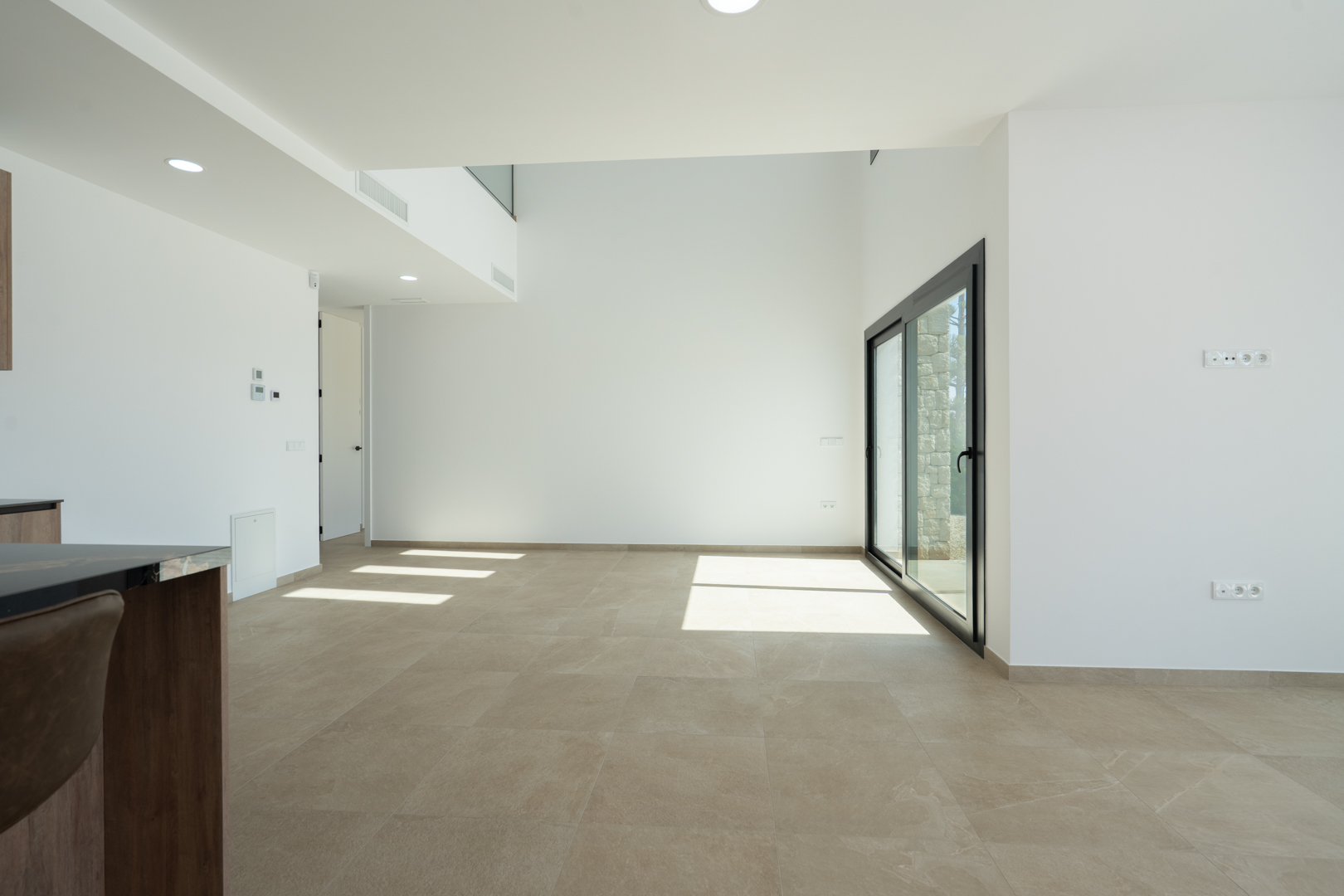 Open woon- en eetkamer met dubbelhoog plafond, grootformaat porseleinen vloertegels en schuifpuien die zorgen voor een natuurlijke lichtinval.