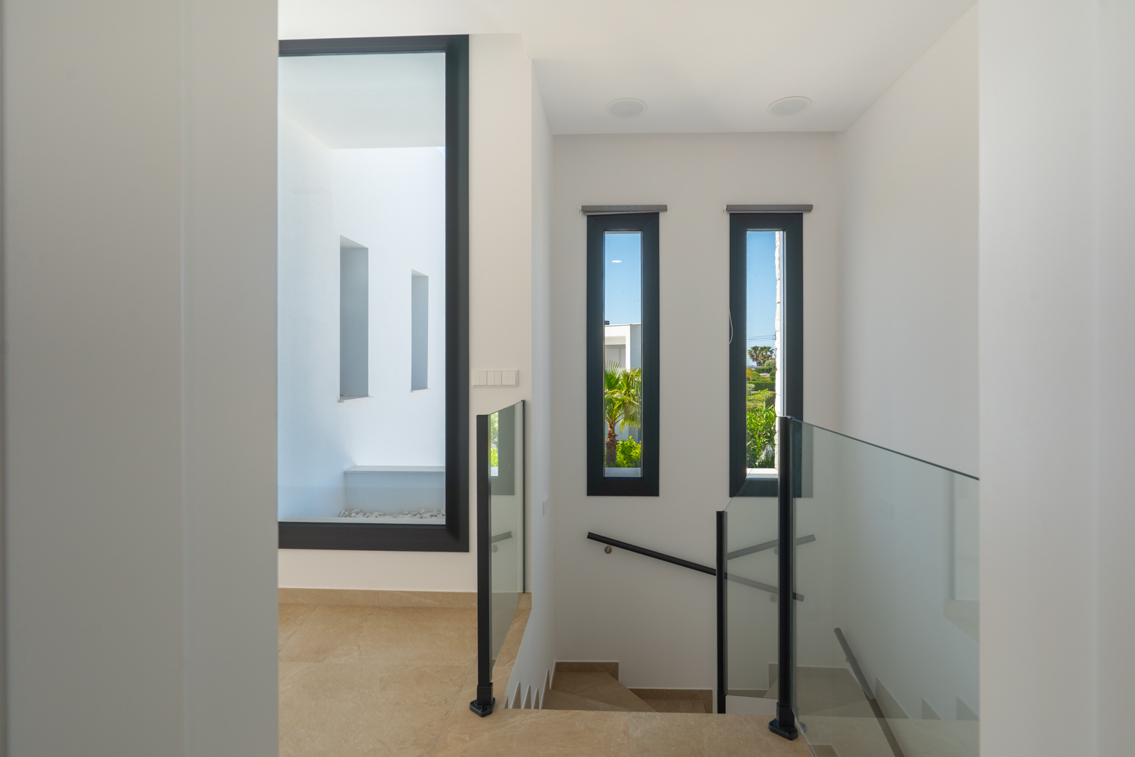 Overloop op de bovenverdieping met glazen balustrades, porseleinen vloeren en grote raampartijen die zorgen voor natuurlijk licht en zicht op de tuin.