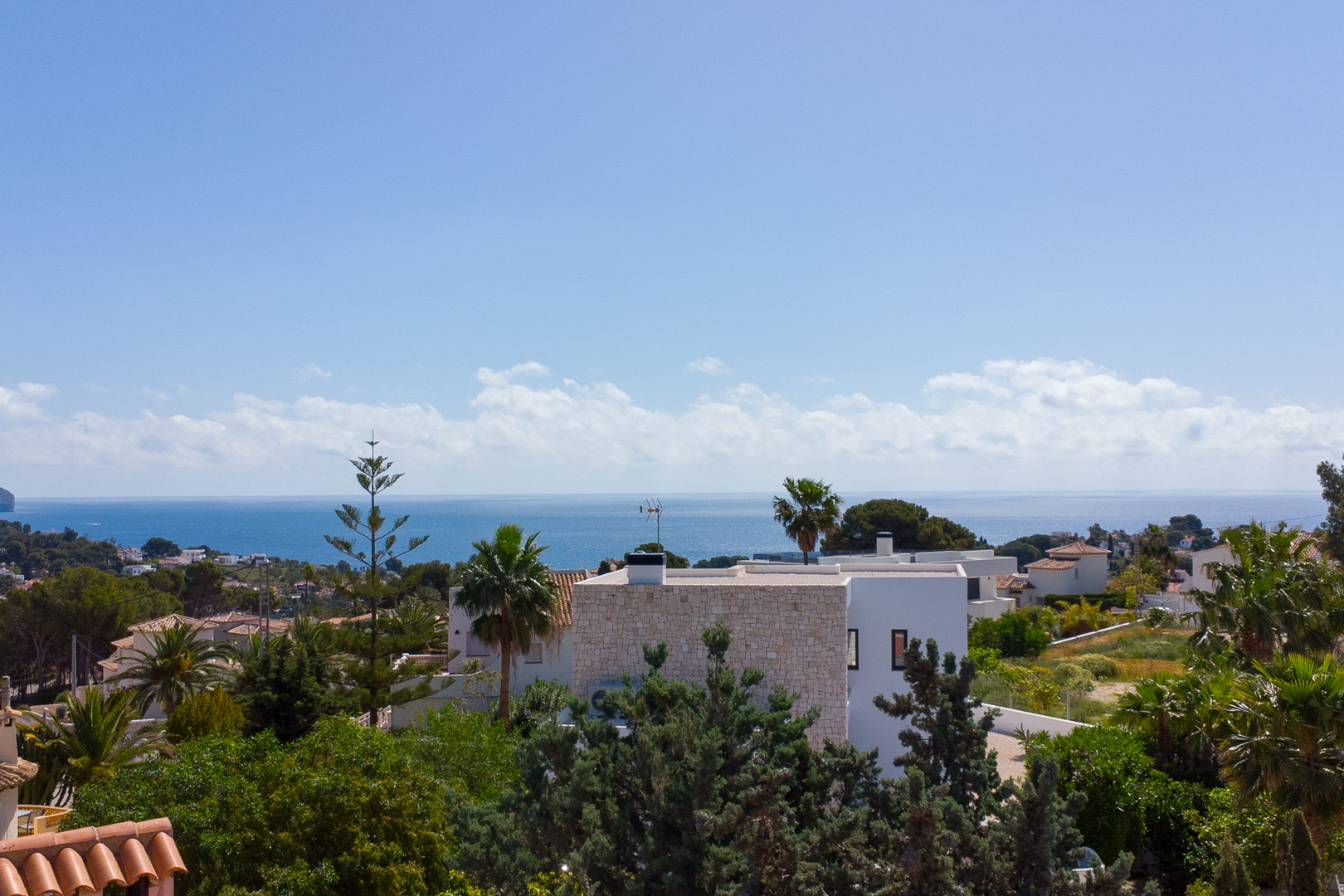 Panoramisch uitzicht vanaf het perceel op de Middellandse Zee, met witte villa's en weelderige mediterrane beplanting onder een heldere lucht.