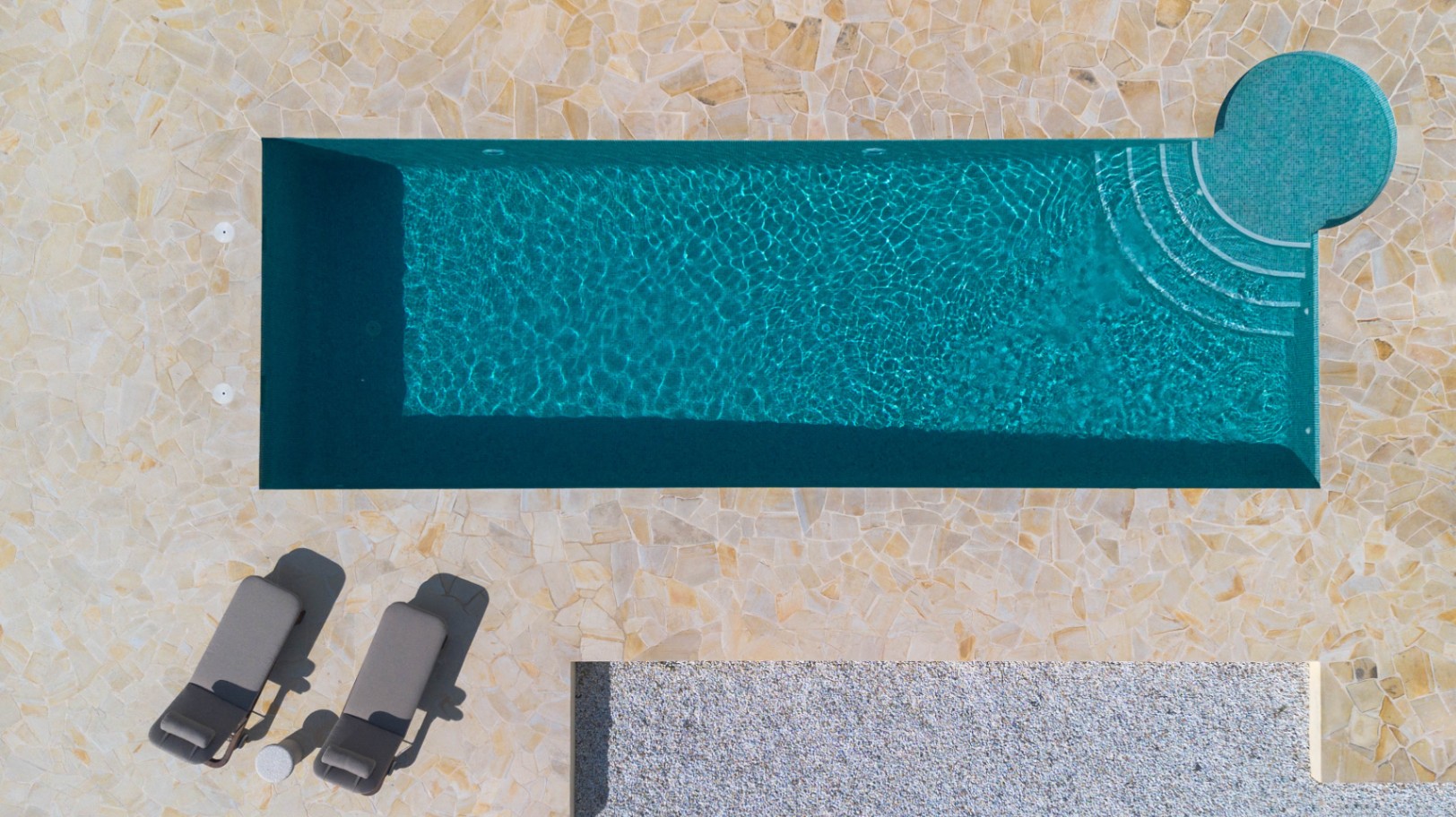 Bovenaanzicht van het 13 meter lange zwembad met turquoise mozaïek, geïntegreerde ronde trap en een terras van onregelmatige natuurstenen tegels.