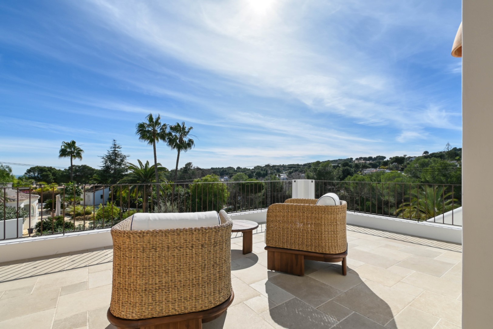 Bovenliggend terras met natuurstenen tegels en rotan fauteuils, met een panoramisch uitzicht op de groene omgeving en palmbomen.