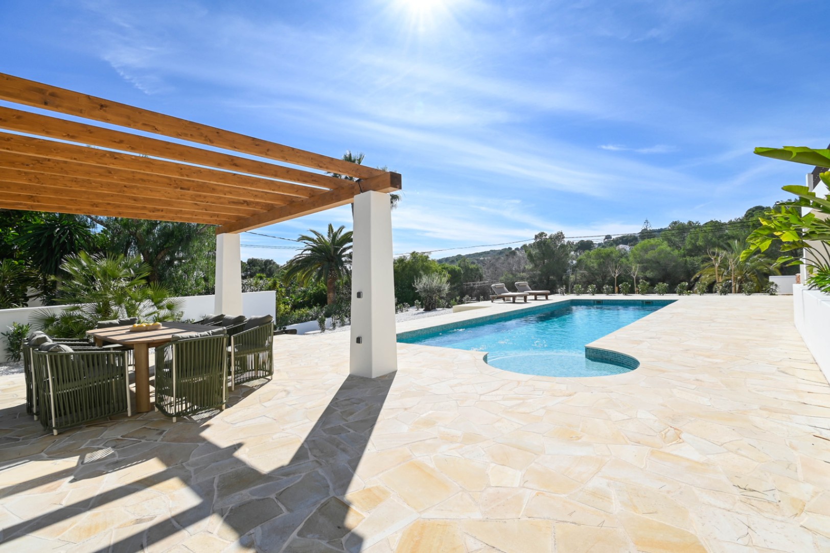 Buitenterras met natuurstenen bestrating, een houten pergola met eethoek en een zwembad van 13 meter omgeven door mediterrane beplanting.