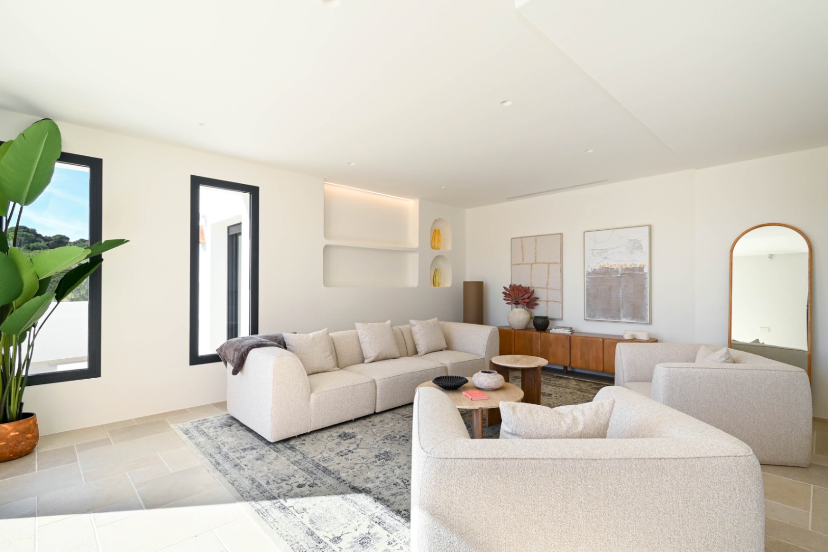 Lichte woonkamer met modulaire banken in neutrale tinten, geïntegreerde wandnissen met ledverlichting en een natuurstenen vloer die rust en luxe uitstraalt.
