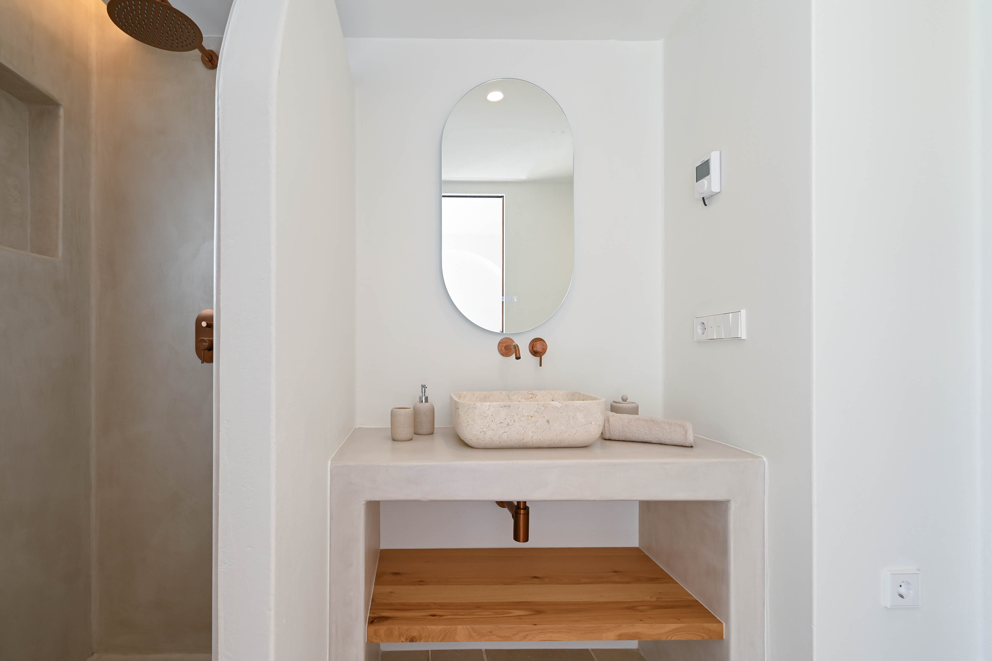 Moderne badkamer met microcement afwerking, natuurstenen waskom en koperkleurige kranen. Voorzien van een houten legplank en een strakke inloopdouche.