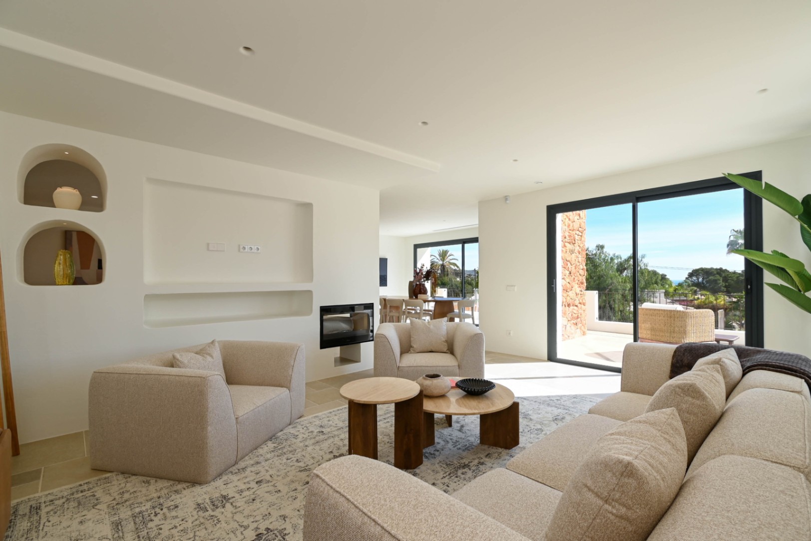 Moderne woonkamer met geïntegreerde haard, minimalistische nissen en grote schuifdeuren die de binnenruimte verbinden met het zonnige terras.