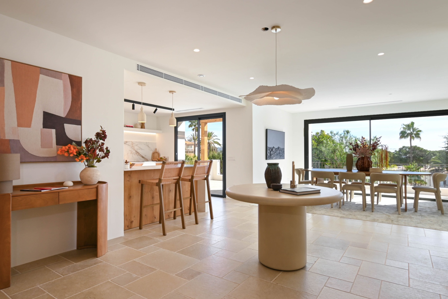Open woonruimte met natuurstenen vloer, geïntegreerde keuken met houten eiland en een lichte eetkamer met grote glazen schuifdeuren die toegang bieden tot het terras.