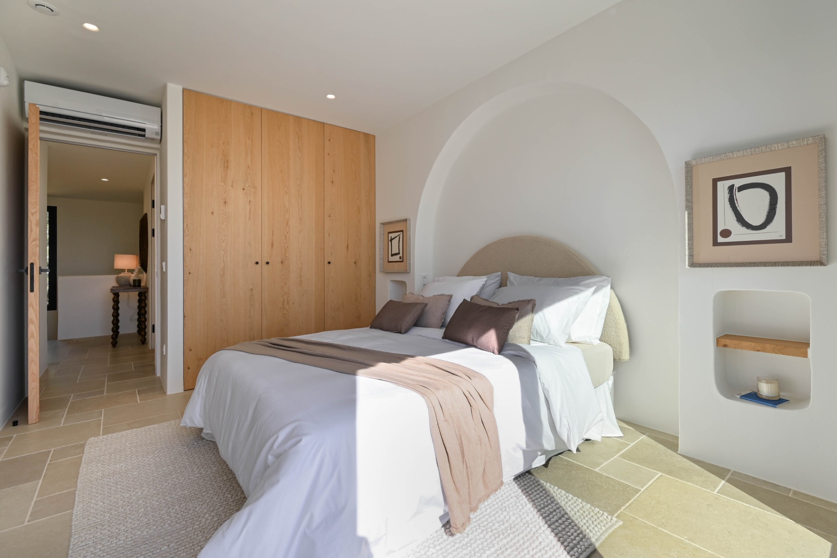 Slaapkamer met ingebouwde houten kasten, natuurstenen vloer en een stijlvolle boognis boven het bed. Voorzien van airconditioning en minimalistische details.