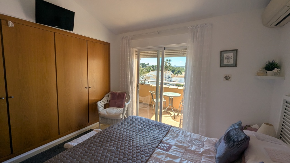 Hoofdslaapkamer met een grote houten inbouwkast, airconditioning en schuifpui naar een privéterras met weids uitzicht over de omgeving.
