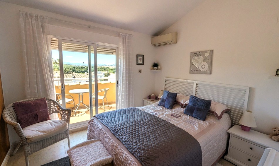 Lichte hoofdslaapkamer met schuin plafond, airconditioning en schuifpui naar een privéterras met weids uitzicht op de bergen en omgeving.