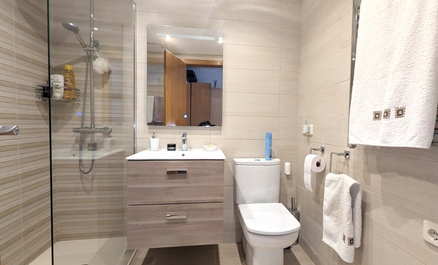 Moderne badkamer met glazen inloopdouche, zwevend wastafelmeubel in lichte houtkleur en wandtegels met horizontale lijnen in neutrale tinten.