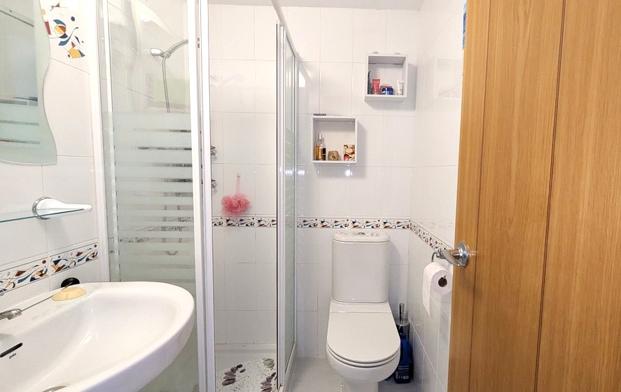 Moderne doucheruimte met witte wandtegels, een decoratieve bies, een glazen douchecabine en wandplanken voor extra opbergruimte.