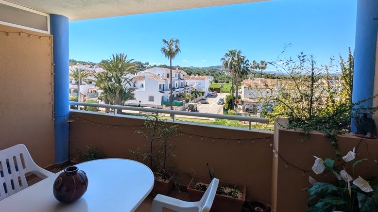 Overdekt terras met eethoek en vrij uitzicht op mediterrane villa's, palmbomen en het Montgó-gebergte in de verte.