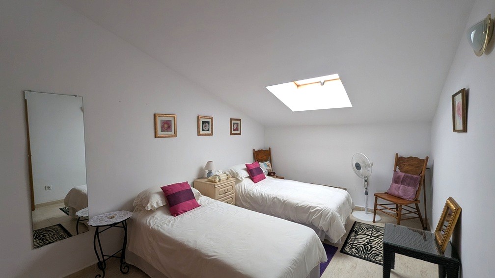 Slaapkamer met schuin plafond, twee eenpersoonsbedden, een dakraam voor natuurlijke lichtinval en een lichte tegelvloer.