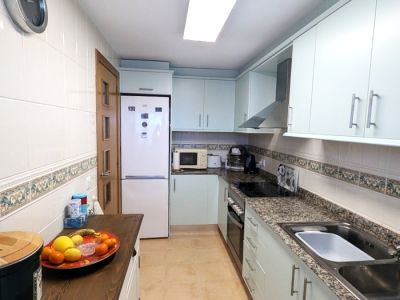 Functionele galerijkeuken met lichtblauwe kasten, gespikkelde granieten werkbladen en witte tegelwanden met decoratieve rand. Voorzien van kookplaat, oven en roestvrijstalen spoelbak.