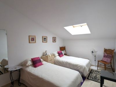 Lichte tweepersoonskamer met schuin plafond en dakraam voor natuurlijk licht. Voorzien van twee eenpersoonsbedden, een nachtkastje en tegelvloer.