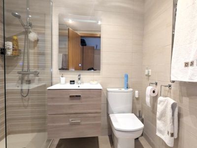 Moderne badkamer met inloopdouche, glazen scherm en gestreepte beige tegels. Een zwevend wastafelmeubel met twee lades en verlichte spiegel completeert de ruimte.