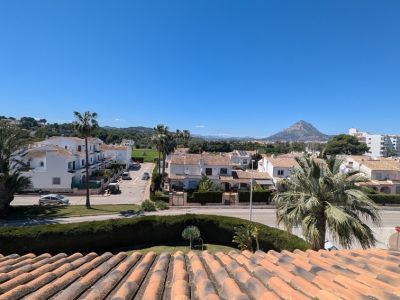 Panoramisch uitzicht vanaf het terras, met terracottadaken, residentiële straten, weelderige palmbomen en de majestueuze Montgó-berg onder een helderblauwe lucht.